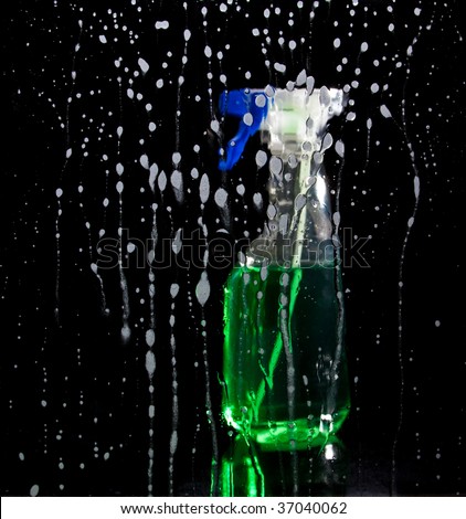 Drops of cleaning agent on glass surface, with unfocused bottle on background