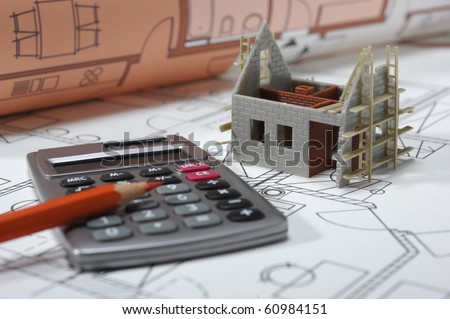house under construction with blue print and calculator