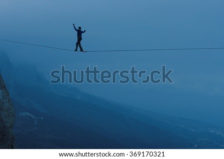 Fearless highliner walking on tight rope. At the height of mountains in the background