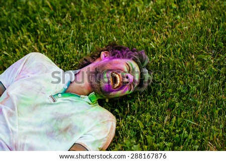 A young man laughing lying on grass. Holi color festival