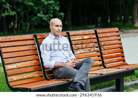 Portrait of a bald and brutal man. Bald man sitting on a bench in the park