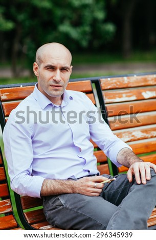 Portrait of a bald and brutal man. Bald man sitting on a bench in the park