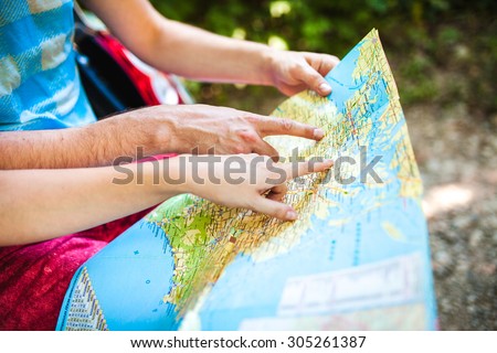 Hands closeup of a young traveler looking at a map while sitting in car trunk