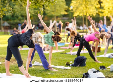 big group of adults attending a yoga class outside in park