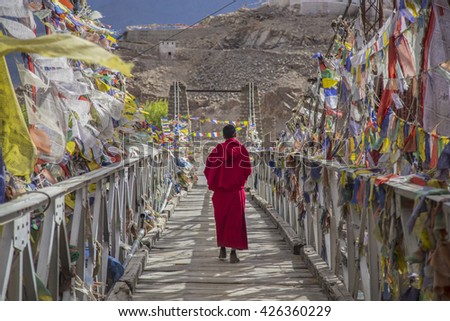 A monk walks onthe bridge pathway surrounded by colorful tibetan prayer flags , Ladakh , India