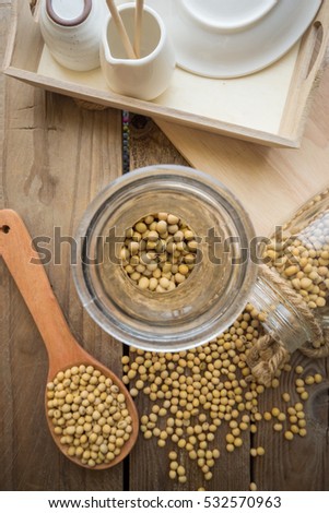 Jar of soybean on wood table with soybean in wood spoon.