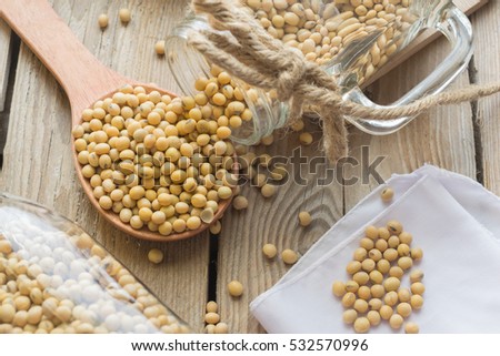Jar of soybean pouring bean into a wood spoon on wood table