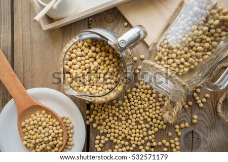 Jar of soybean pouring bean into a wood table with soybean in wood spoon.