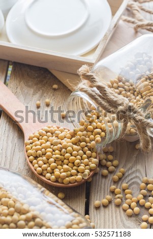 Jar of soybean pouring bean into a wood spoon on wood table