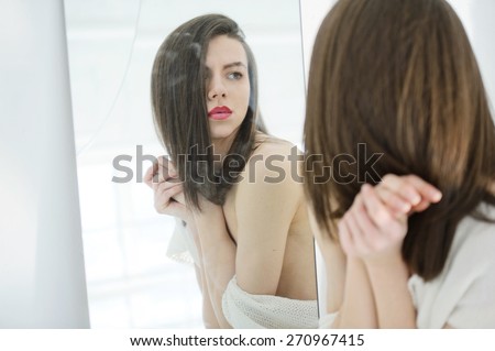 Androgynous beautiful young man like a beautiful woman with red lipstick looks in a mirror