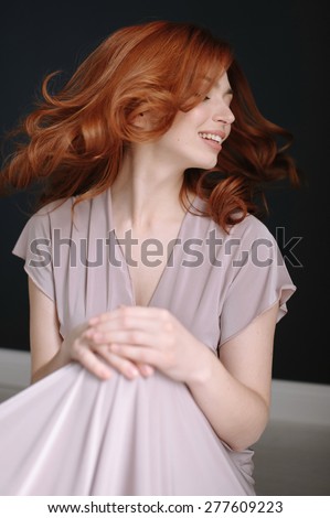 Portrait of a smiling beautiful red-haired (ginger) girl posing in studio. Healthy long and wavy hair. Daylight.