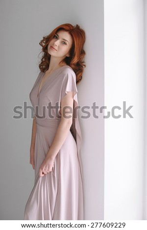 Portrait of a smiling beautiful red-haired (ginger) girl posing in studio. Healthy long and wavy hair. Daylight.