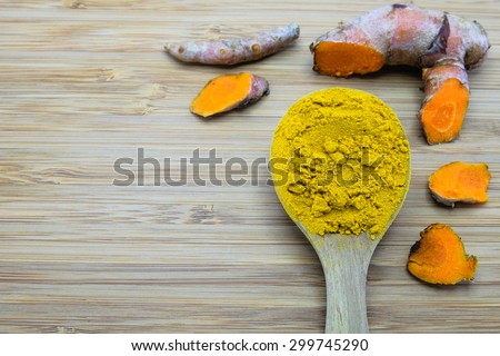 turmeric powder in wood spoon and turmeric root on wood background
