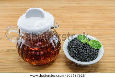 sesame oil in glass jug and black sesame seeds in bowl on wood background