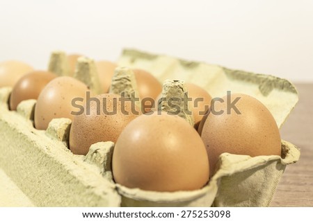 Eggs, ten brown eggs in a carton package on a wooden table, close up