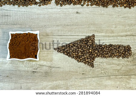 Arrow from the coffee beans with a cup of fresh ground coffee on wooden background