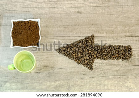 Arrow from the coffee beans with a cup of fresh ground coffee and empty cup on wooden background