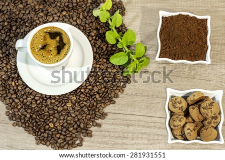 Cup of fresh coffee, coffee beans,  fresh ground coffee, cookies with chocolate and mint leaves on wooden table
