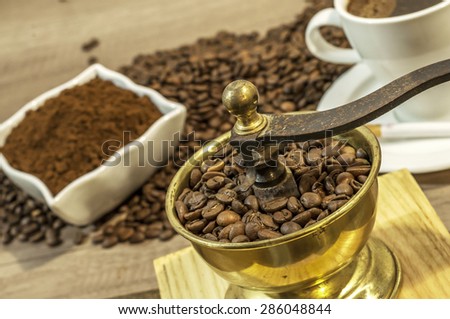 Coffee grinder with coffee beans, cup of coffee and ground coffee in bowl on wooden table