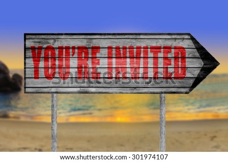 Red You\'re Invited! wooden sign with a beach on background