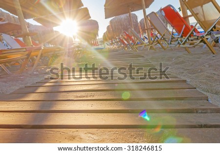 Sunbed, straw umbrella on beautiful beach background with burning sun