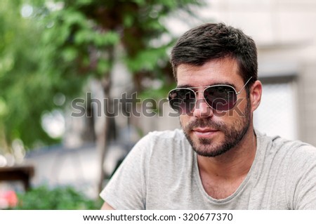Portrait of a young handsome man, model of fashion, wearing tinted sunglasses in city background