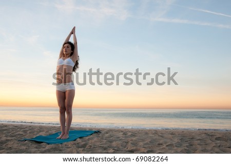 Young beautiful woman practicing yoga at sunrise on the beach by the ocean