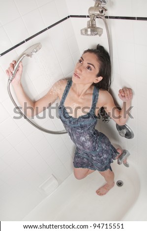 Beautiful model wearing a wet blue dress inside a white bathtub taking a relaxing shower and washing her hair