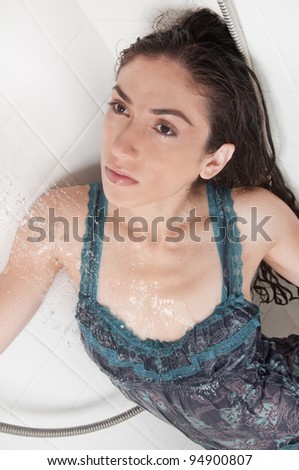 Beautiful model wearing a wet blue dress inside a white bathtub taking a relaxing shower and washing her hair