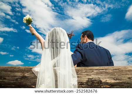 Back view of bride and groom. Bride is lifting the bouquet of flowers trough the sky. Clouds are very dramatic.