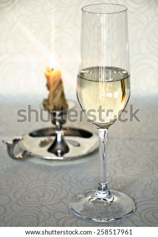 The cup of white wine with the candle in the background