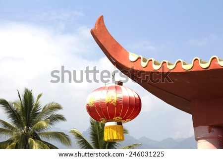 Red Chinese Lantern hanging on edge of concrete roof against blue sky and coconut tree