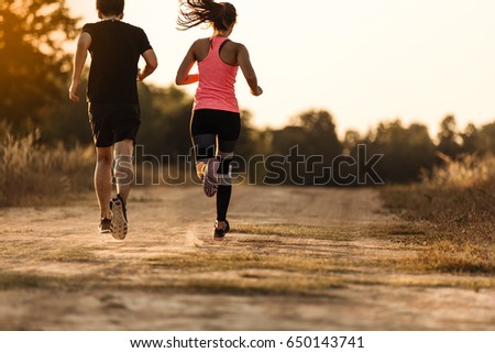 Young couple running at forest trail. stretching before fitness training session at the park. Healthy young woman warming up outdoors. She is stretching her arms and looking away,hi key.