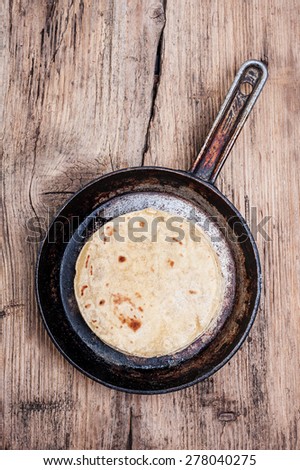 fried tortilla made of corn flour in a cast iron skillet on textured wooden background
