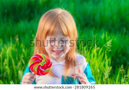 beautiful red-haired girl with freckles holding a Lollipop and hide his eyes from pleasure on the background of green grass
