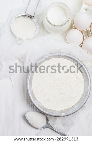 wheat flour in the iron bowl, cream in a glass jar, chicken eggs, sugar - ingredients for the dough, top view
