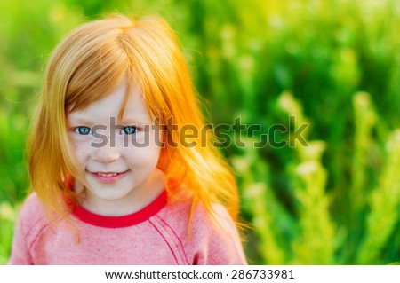 portrait of beautiful red-haired girl with big blue eyes and a sweet smile on background of green grass