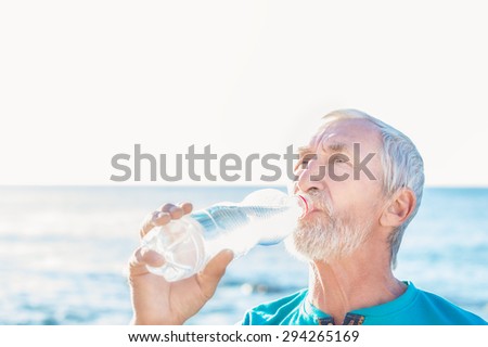 beautiful silver-haired man with a beard drinking water on the background of blue sea and sky
