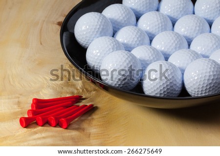 Black ceramic bowl full of white golf balls on a wooden desk
