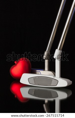 Two different golf putters and red heart  on a black glass desk