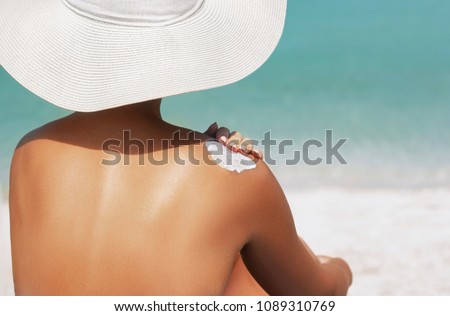 Woman applying sunscreen creme on  tanned  shoulder. Skincare. Body Sun protection suncream. Bikini hat woman applying moisturizing sunscreen lotion on back.