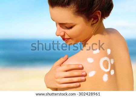 Portrait of gorgeous young woman smiling  in bikini with the drawn sun on a shoulder at beach