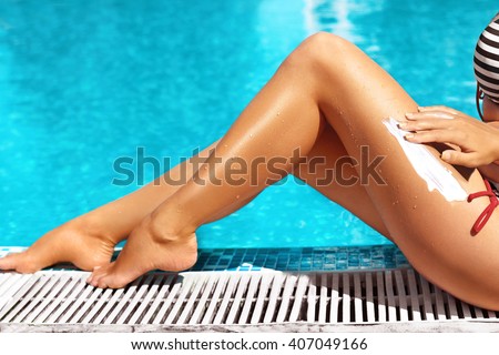 Woman apply sun protection cream on her smooth tanned legs.Beautiful  legs outdoors by pool under sunshine on beautiful summer day.