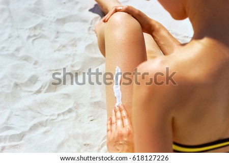 Closeup on female Hand applying sunscreen creme on Leg. Skincare. \
Sun protection sun cream, on her smooth tanned legs.