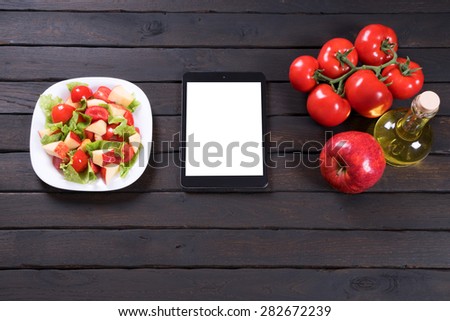 Salad with tomatoes apples and lettuce next to the tablet computer. Dark background.
