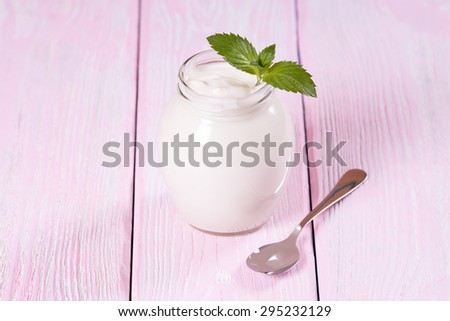 Low-fat yogurt in a glass jar with a spoon. Pink background.
