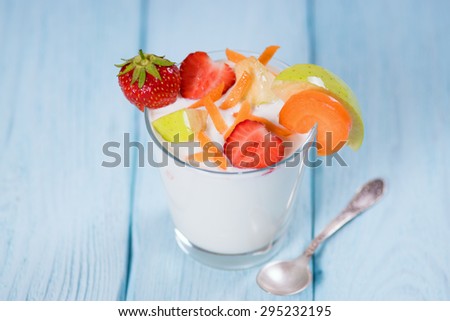 Yogurt with strawberries apples and carrot in a glass. Blue background.