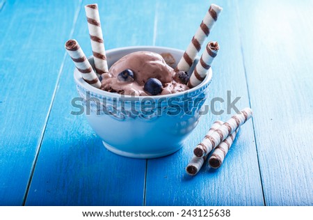 Chocolate ice cream with blueberries and wafer rolls on a blue table