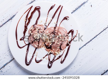 Chocolate ice cream with cashews and chocolate syrup on white table