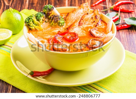 Thai Tom Yam soup with chicken, broccoli, mushrooms on a brown wooden background